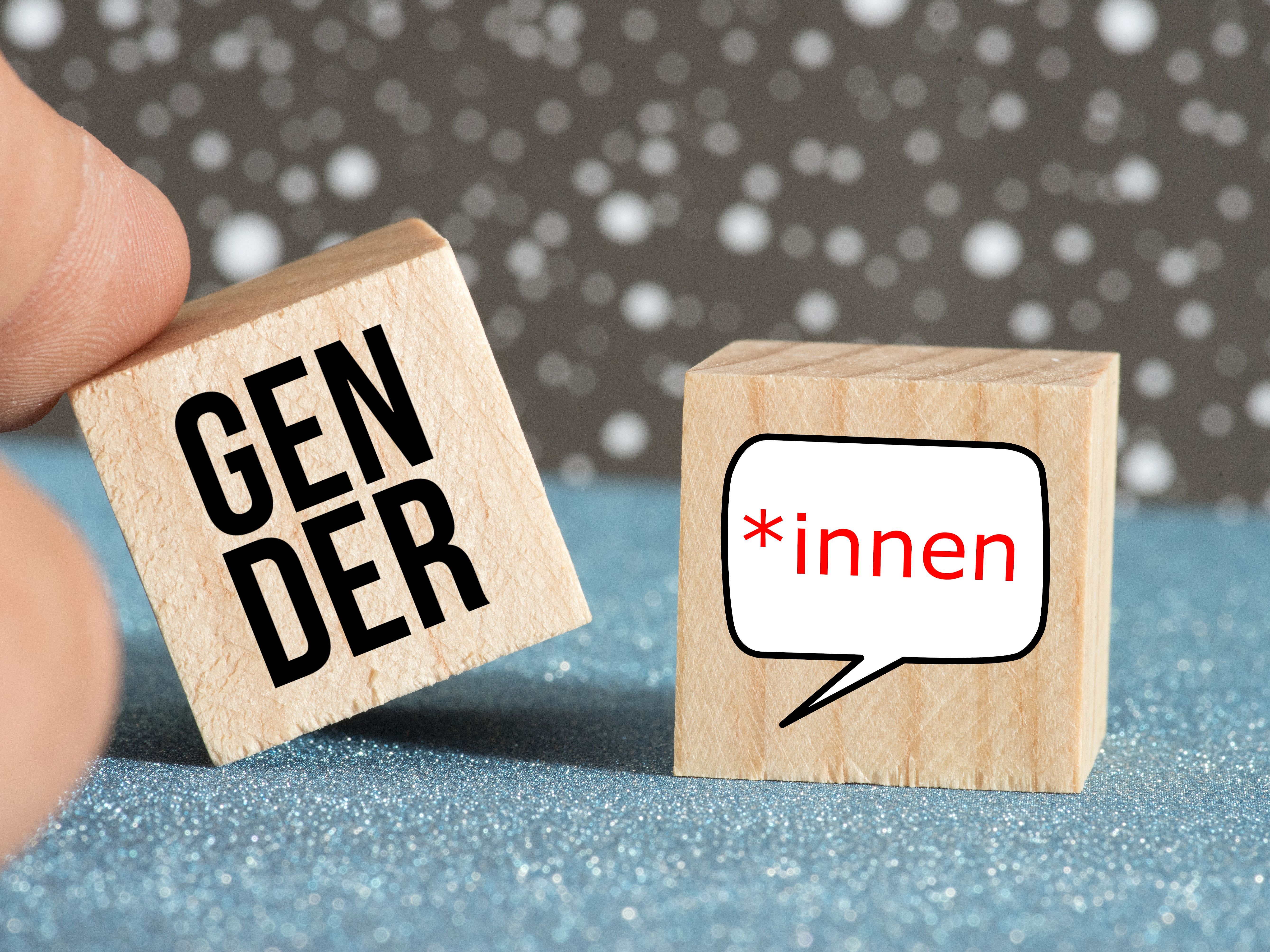 Play tile picture showing fingers, playing with two wooden cubes labelled "Gender" and "*innen" (link to "Gender-sensitive language")