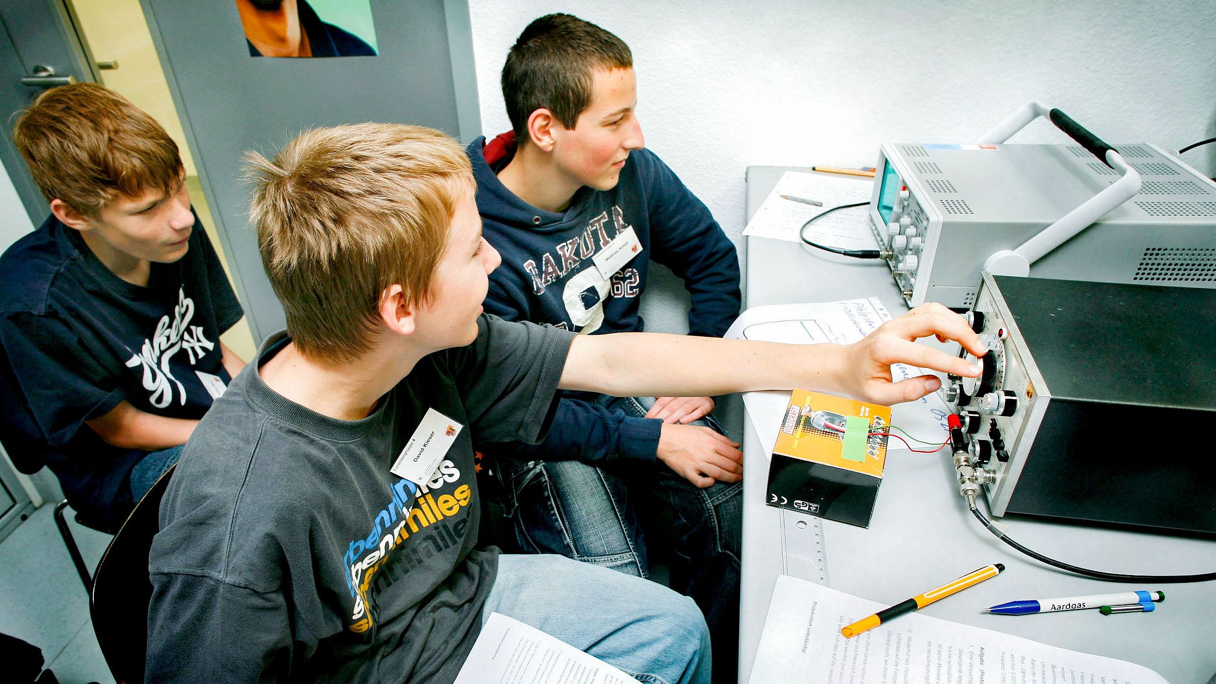 Three young pupils sit in a small room and turn the knobs of an instrument.